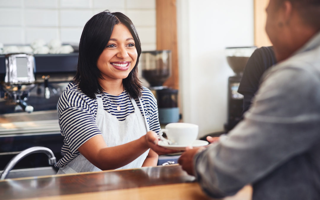 A young barista serving a cup of coffee to a customer in a cafe